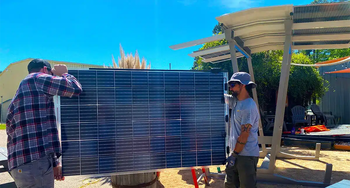 Solar technicians from Southern Energy Management carry a solar panel to install on a new Haven Solar Shelter