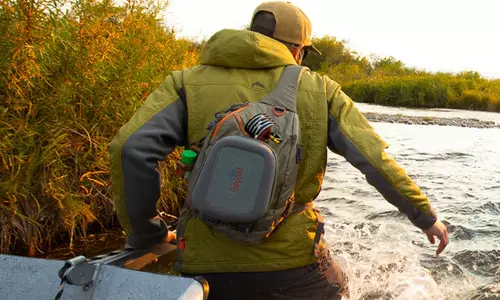 person wearing a submersible fishpond sling and tugging a boat through a river during sunrise