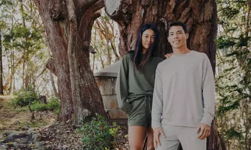 A man and a woman wearing paka clothing outside in the trees